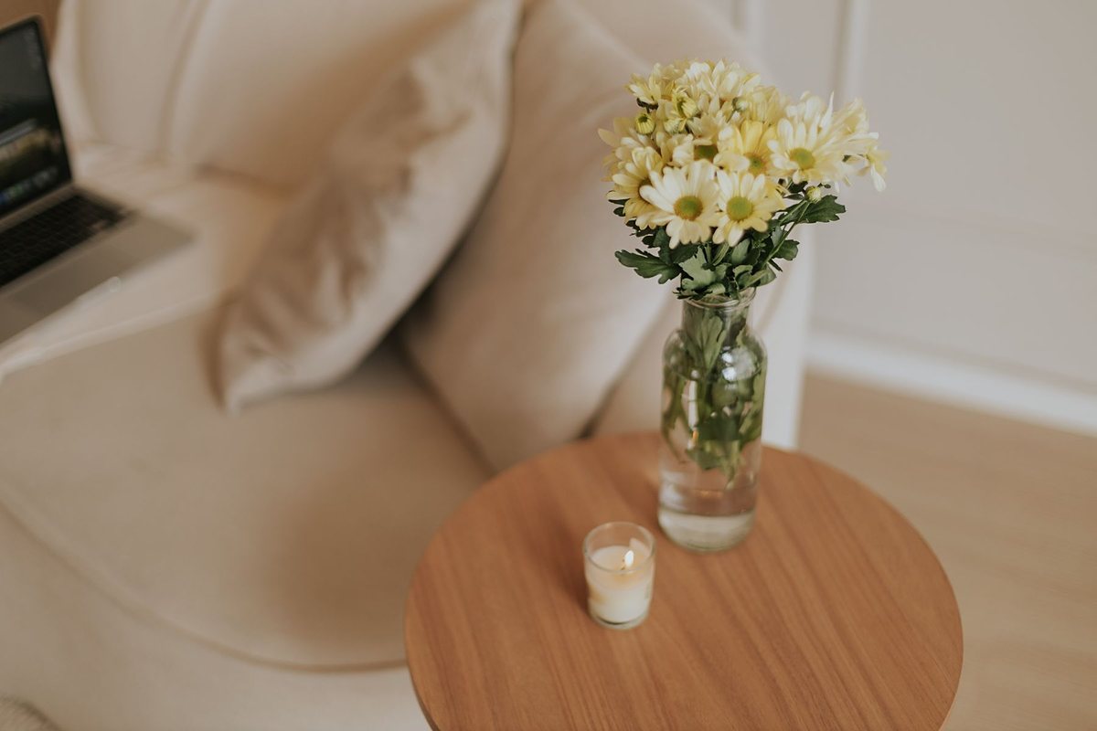 Bình thủy tinh nhỏ cắm hoa cúc trắng vàng trên bàn tròn cạnh ghế sofa